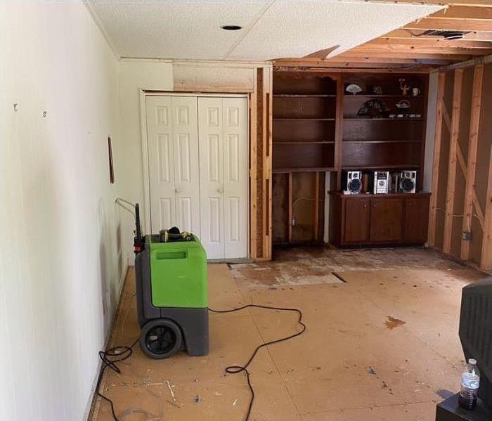 Brown flooring underneath torn up hardwood flooring with a closet and brown built-in bookshelf in the back.