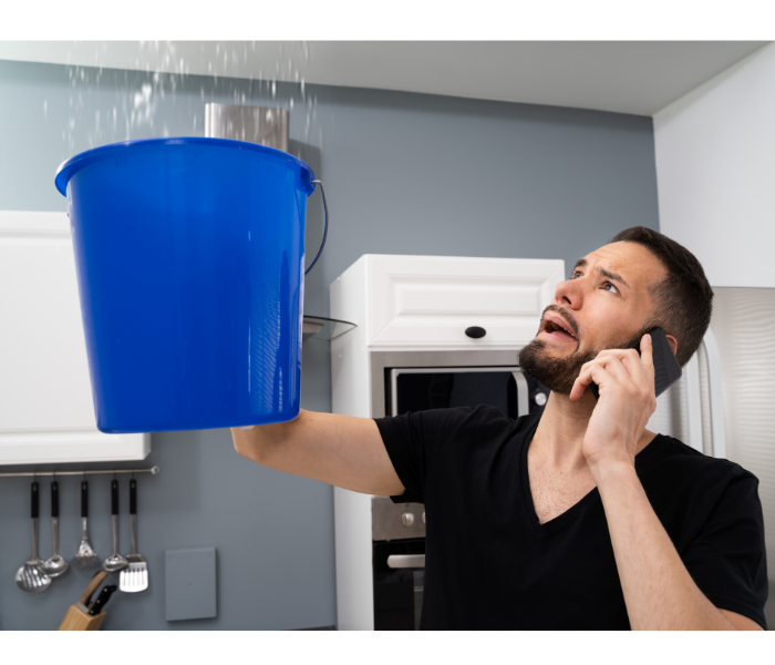 A man with a blue bucket catching water from the ceiling.