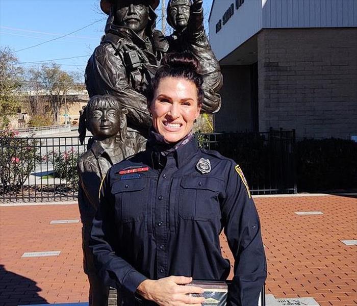 white female firefighter in blue uniform smiling with blue sky and statue behind her